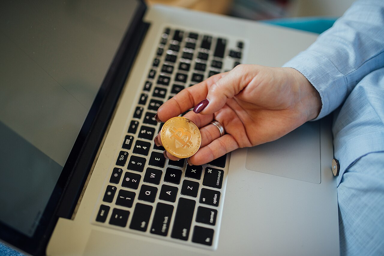 Close-up of a Bitcoin physical coin in a womans hand and a laptop on her lap.jpg